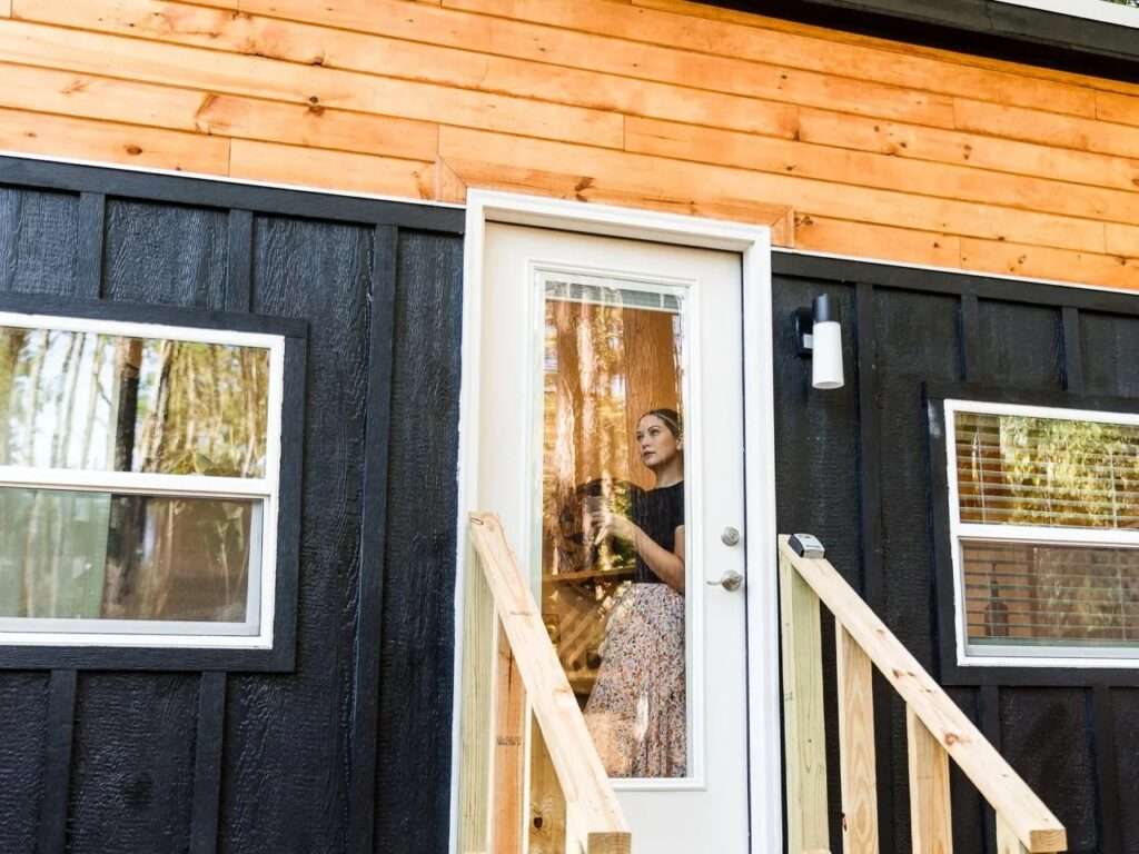 Close-up of the front entrance door and double-hung windows on the dark vertical siding of the Tulsi tiny house by Simplify Further.