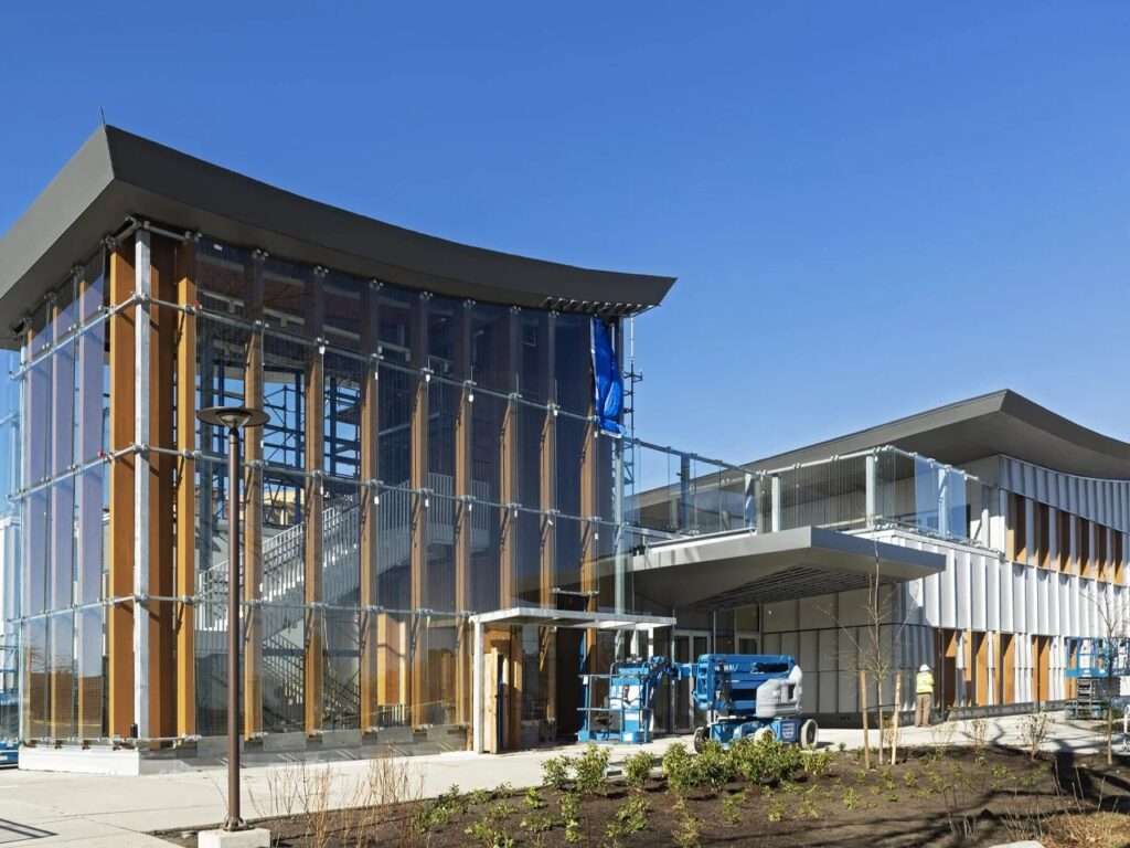 Exterior view of Marpole Community Centre in Vancouver showing the double-height glass facade and exposed Glulam timber columns under a clear blue sky.