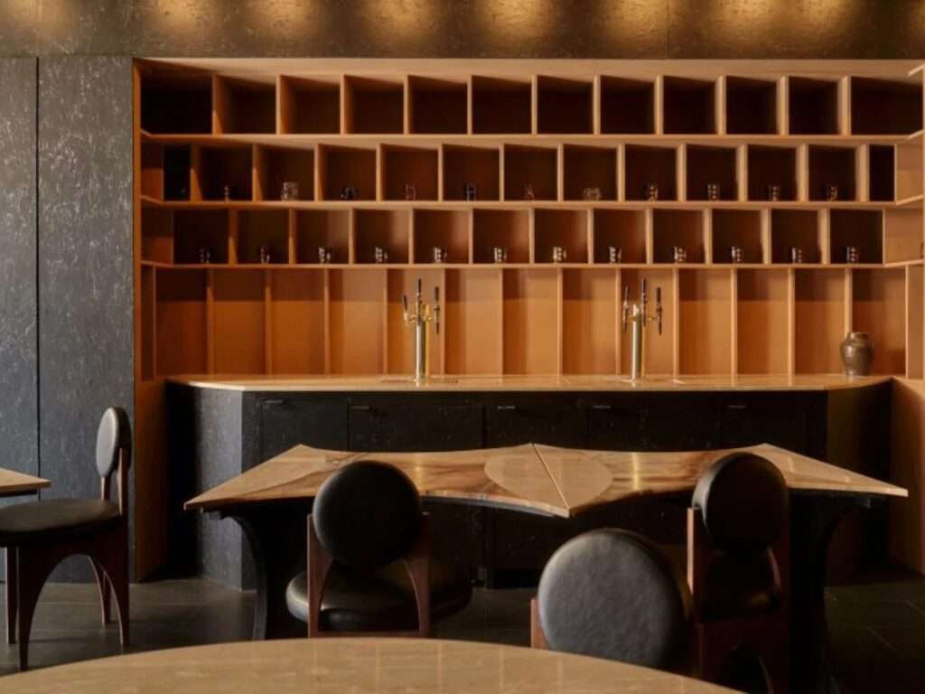 Minimalist wooden shelving unit behind a dark service counter in Gourmega restaurant with lime-washed black walls.