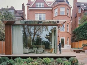 Modern glass extension with polished steel roof and Iroko wood cladding attached to a traditional brick house in Hampstead.