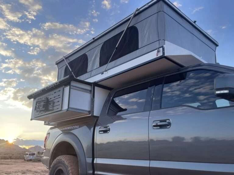 Side view of the grey Roam Rider SL pickup camper with its fabric pop-up roof extended and stainless steel gas struts visible during sunset.