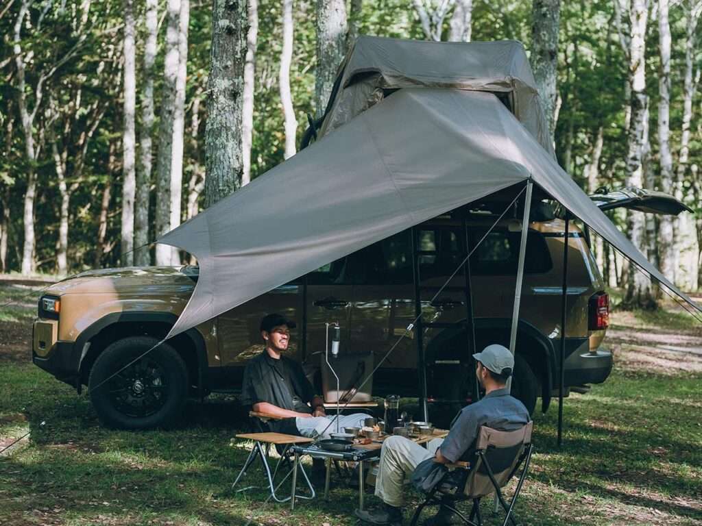 Side view of a vehicle with the Fire Rise RTT deployed and a large side awning creating a shaded outdoor seating area.