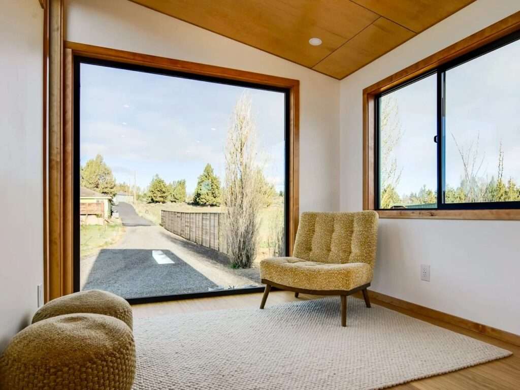 Interior view of the raised living room platform in the Black Butte tiny home, showing an armchair next to a massive floor-to-ceiling picture window.