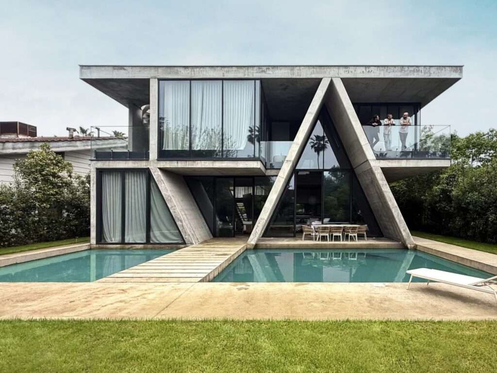 Rear pool view of Gable Villa by Next Office featuring a bold concrete A-frame canopy intersecting a multi-level orthogonal residential structure.
