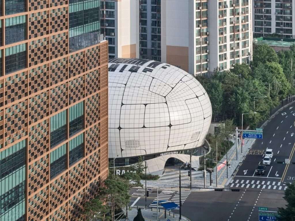 High-angle view of the Seoul Robot and AI Museum nestled within a dense urban landscape of residential high-rises and busy city streets.