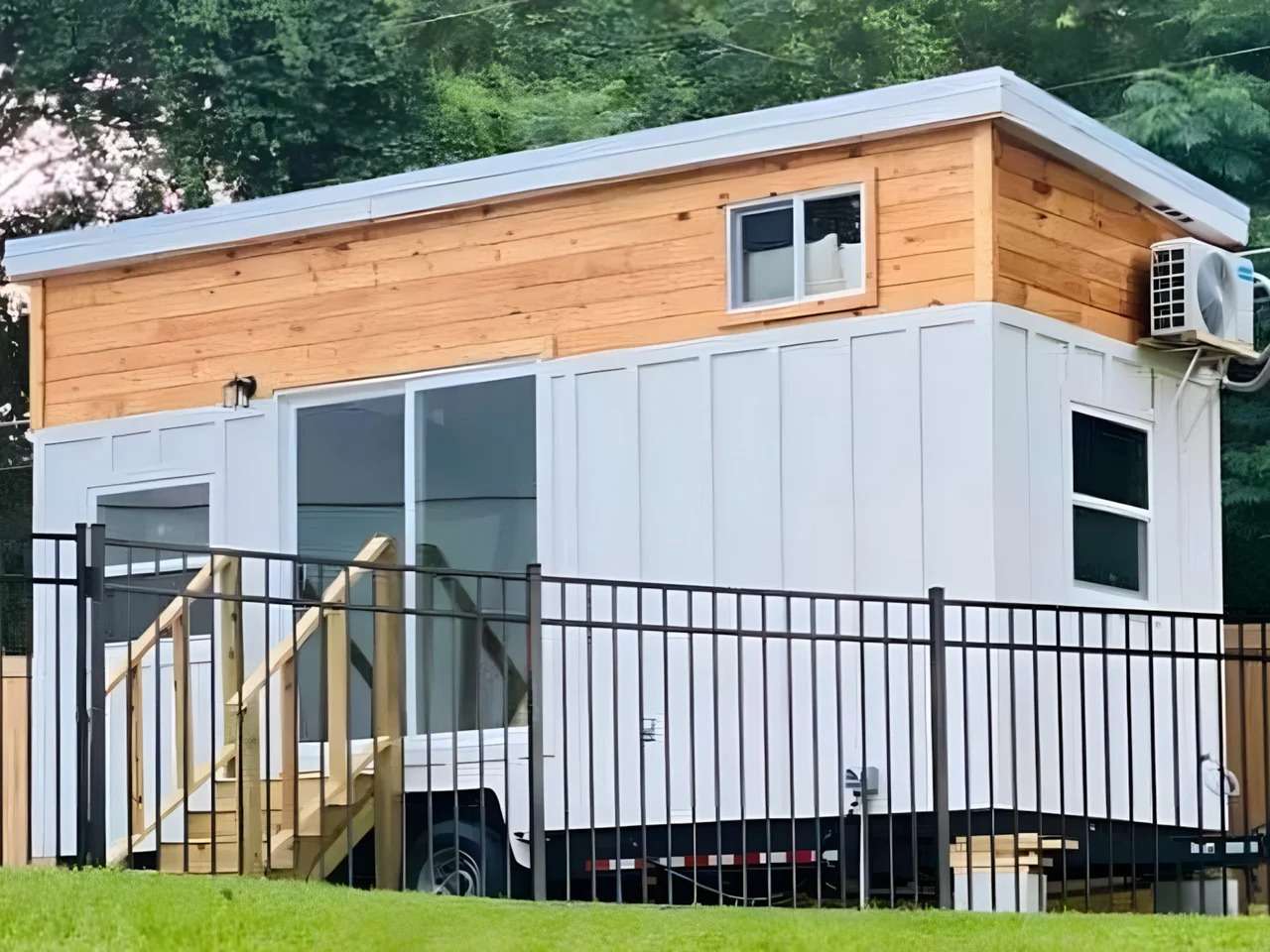 Exterior view of Rasa tiny home on wheels by Simplify Further Tiny Homes featuring white board and batten siding with natural wood accents.