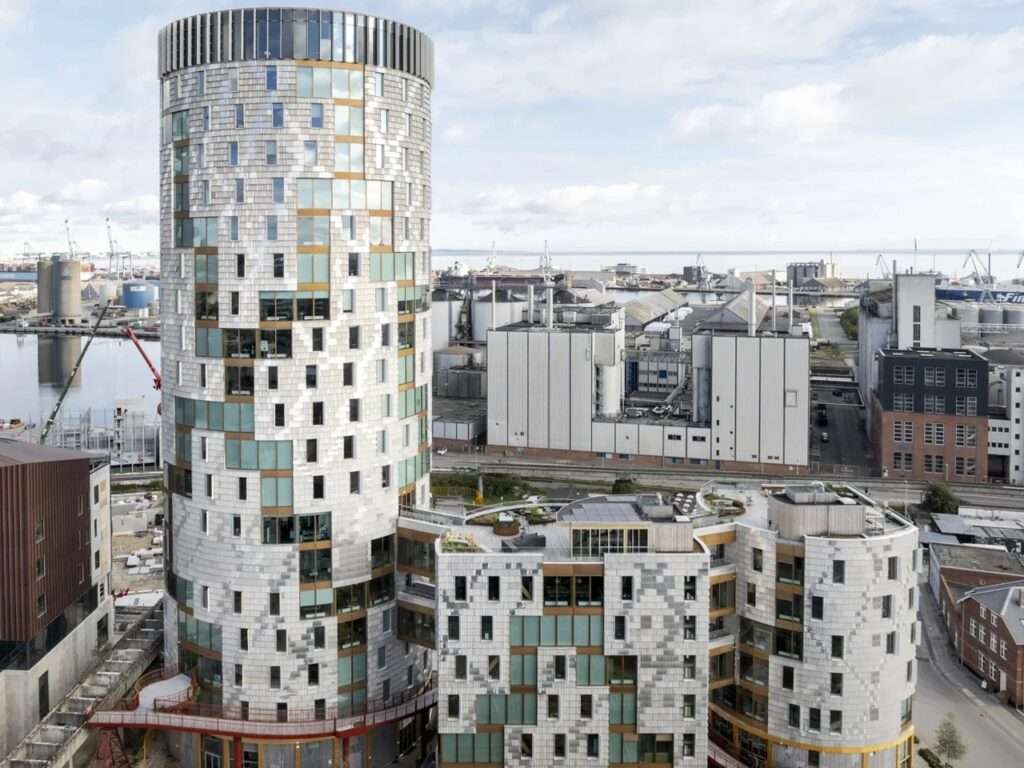 Aerial view of the TRAE timber high-rise building in Aarhus harbor showing its three interconnected architectural volumes and reclaimed aluminum facade.