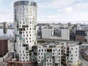 Aerial view of the TRAE timber high-rise building in Aarhus harbor showing its three interconnected architectural volumes and reclaimed aluminum facade.
