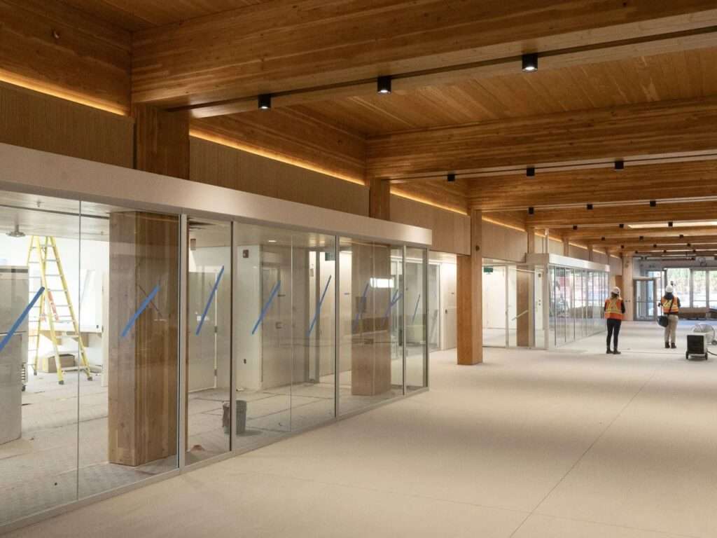 Interior construction phase of Marpole Community Centre featuring exposed CLT ceiling panels, Glulam beams, and glass-walled multipurpose rooms.