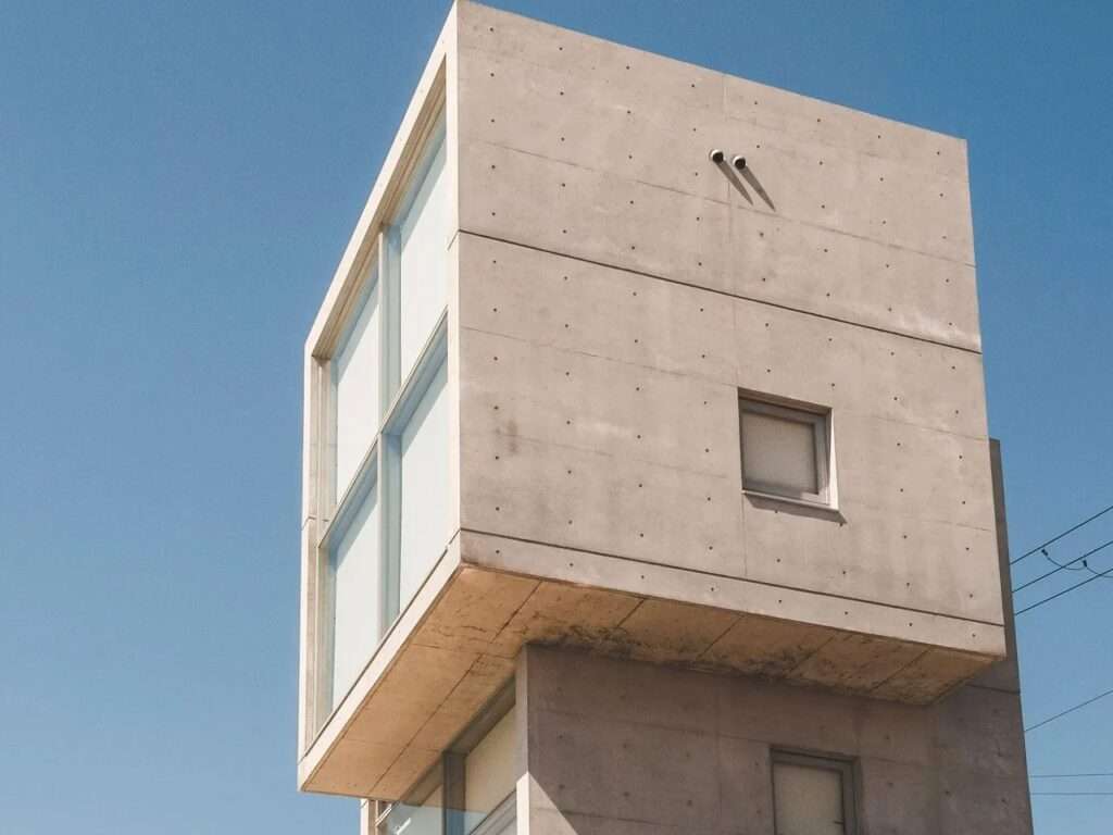 Worm's eye view detail of the concrete 4x4 House top floor cube by Tadao Ando, showcasing the shifting volume offset and large glass grid facade under sunlight.