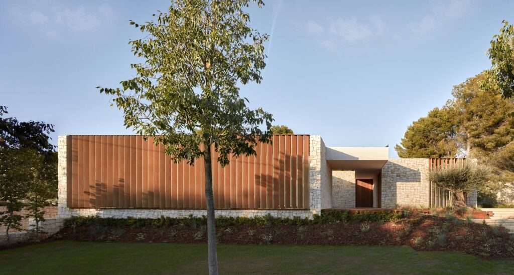 Exterior facade of the house showing stone masonry walls and a large section of vertical adjustable wooden shutters.