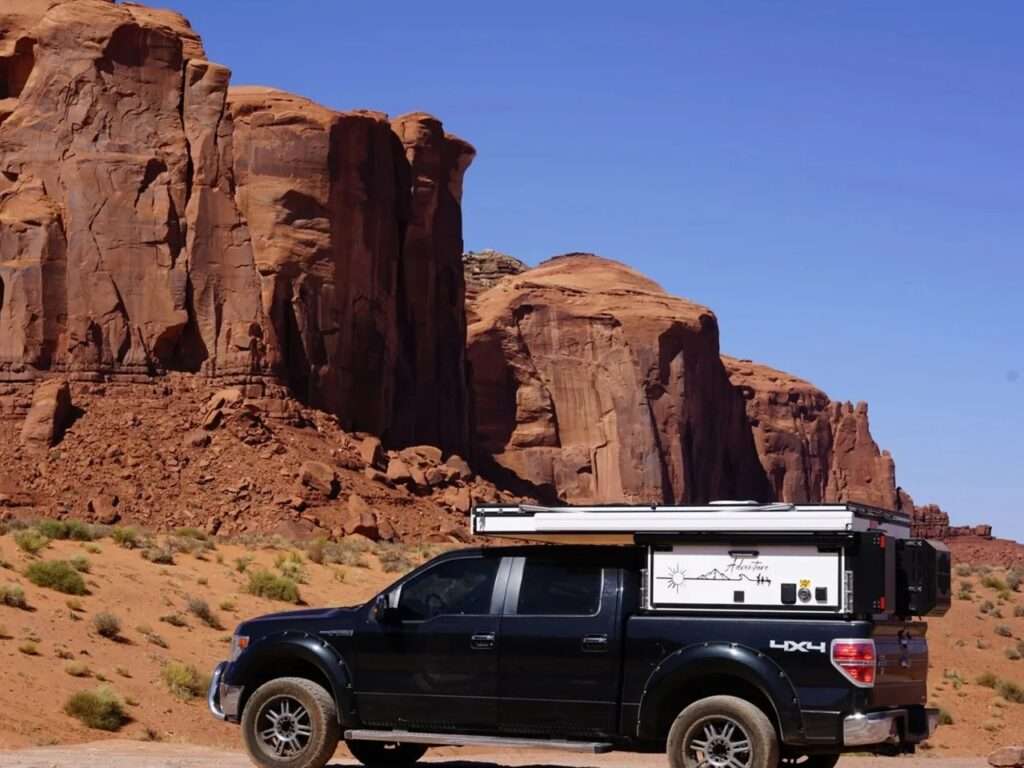 Black pickup truck equipped with the Roam Rider SL camper parked in a desert landscape with large rock formations.
