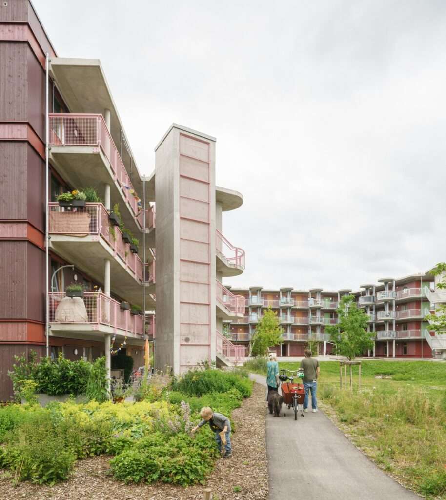 A tall cast-in-place concrete staircase tower and access corridors looking over the central landscaping of the Freiham apartment complex.