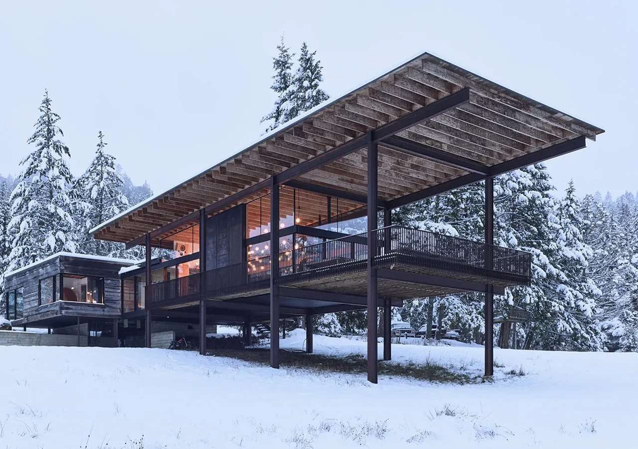 Exterior view of Daisy House in Salt Spring Island during winter, showing the cantilevered roof and steel structure against a snowy landscape.