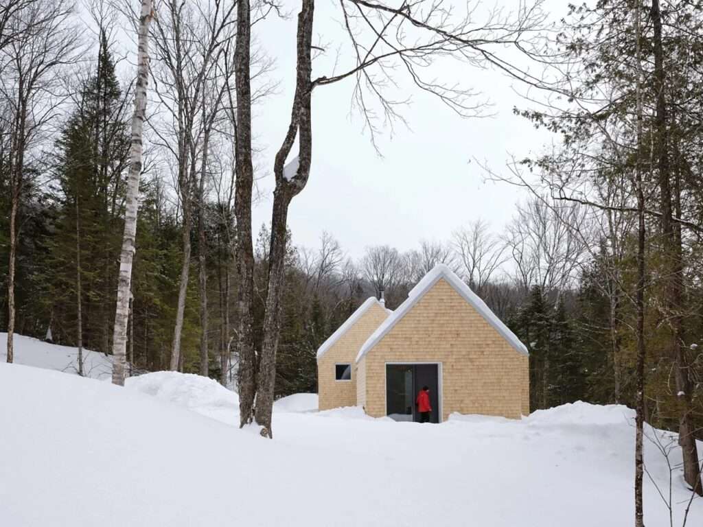 Exterior front view of La Maraude house with cedar shingle siding and gabled roof nestled in a snowy Quebec forest.