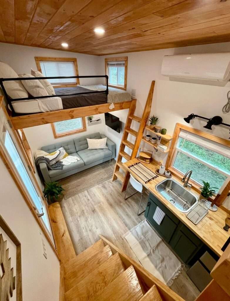 High-angle interior view of Rasa tiny home showing the living area, green kitchen cabinets, and a sleeping loft with a wooden ladder.
