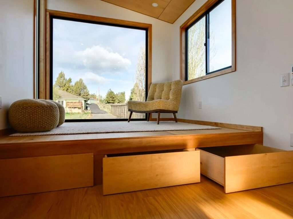 Built-in under-floor storage drawers pulled open beneath the elevated wooden living room platform of the Black Butte tiny home.