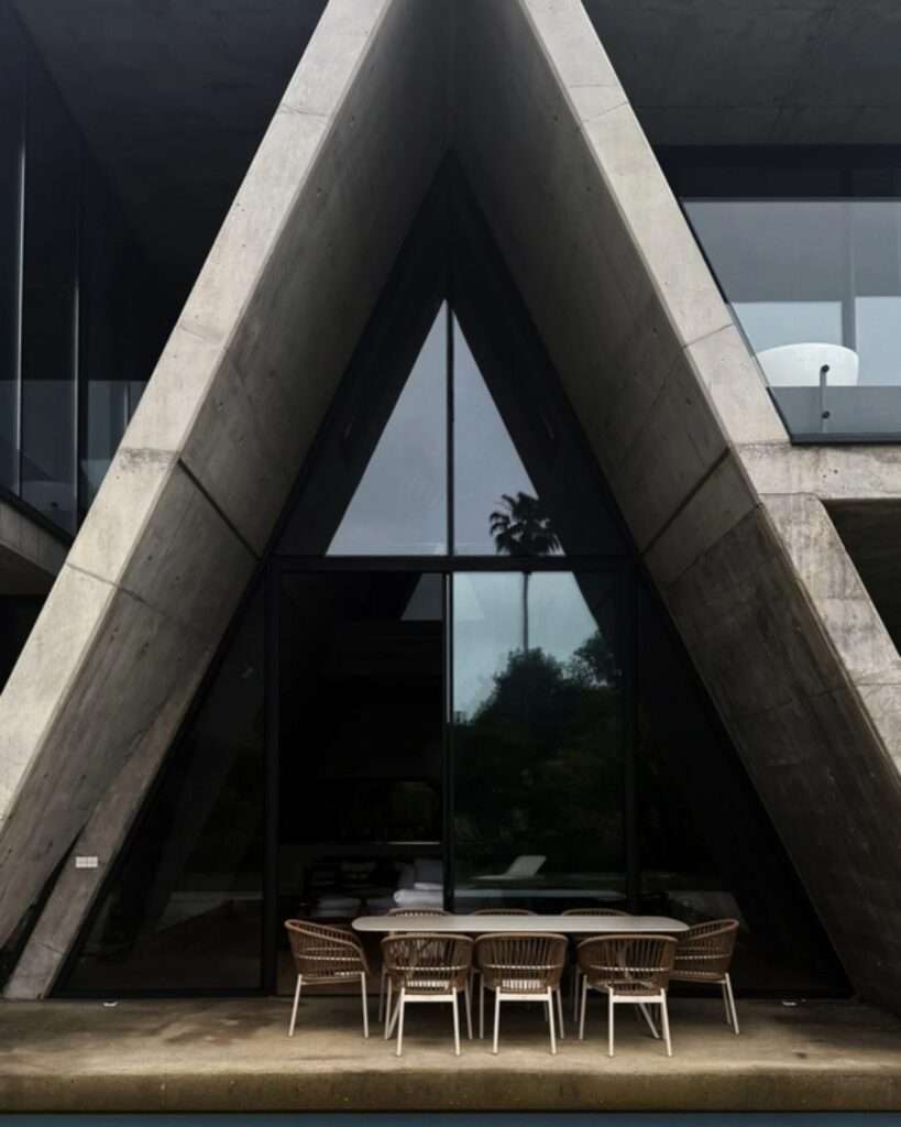 Symmetrical close-up of a concrete A-frame gable canopy sheltering an outdoor dining area by a swimming pool at Gable Villa.