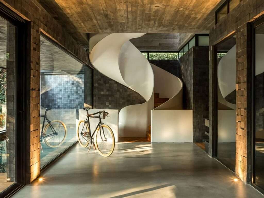 A white sculptural spiral staircase in House 17-JB contrasted against dark stone walls and a exposed concrete ceiling.