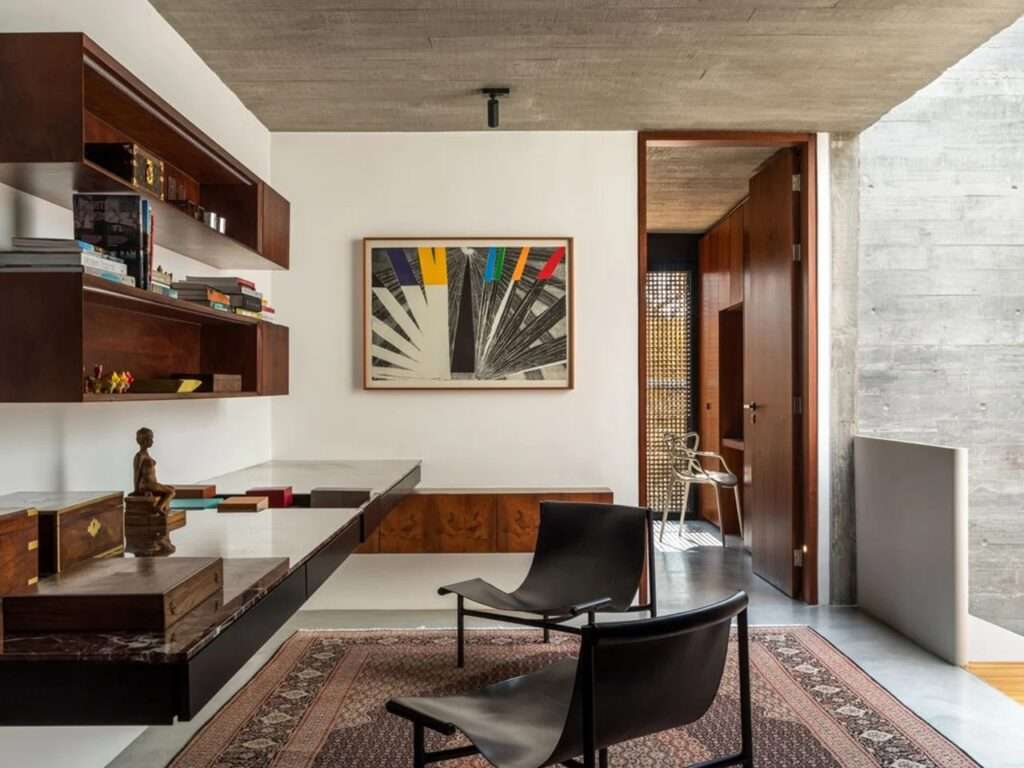 Minimalist home office in House 17-JB with wooden shelving, leather chairs, and a concrete ceiling.