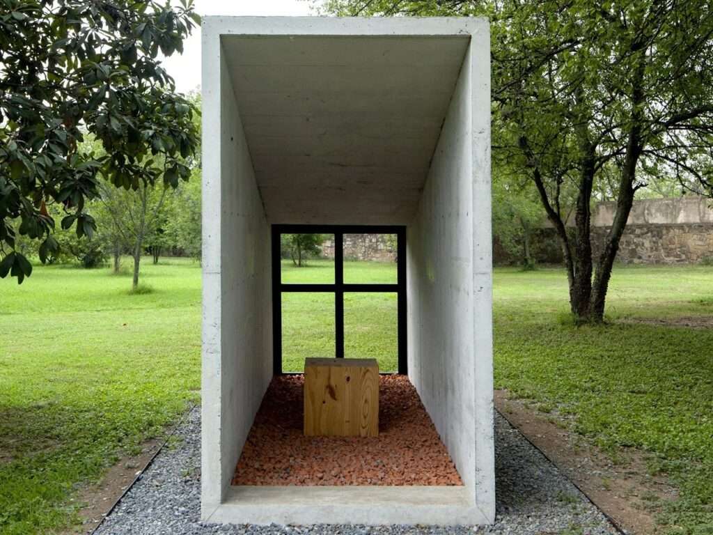 Symmetrical interior view of the Oratory Chapel looking toward a cross-framed window and a simple wooden altar block.