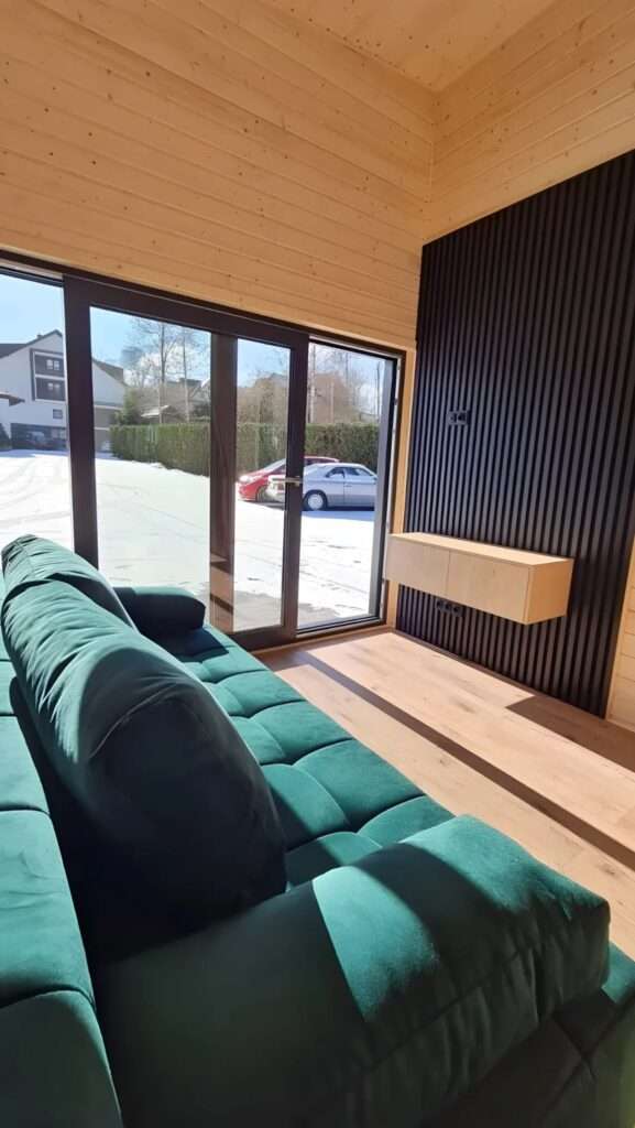Modern tiny house living room with a teal velvet sofa and large sliding glass doors overlooking a snowy landscape.