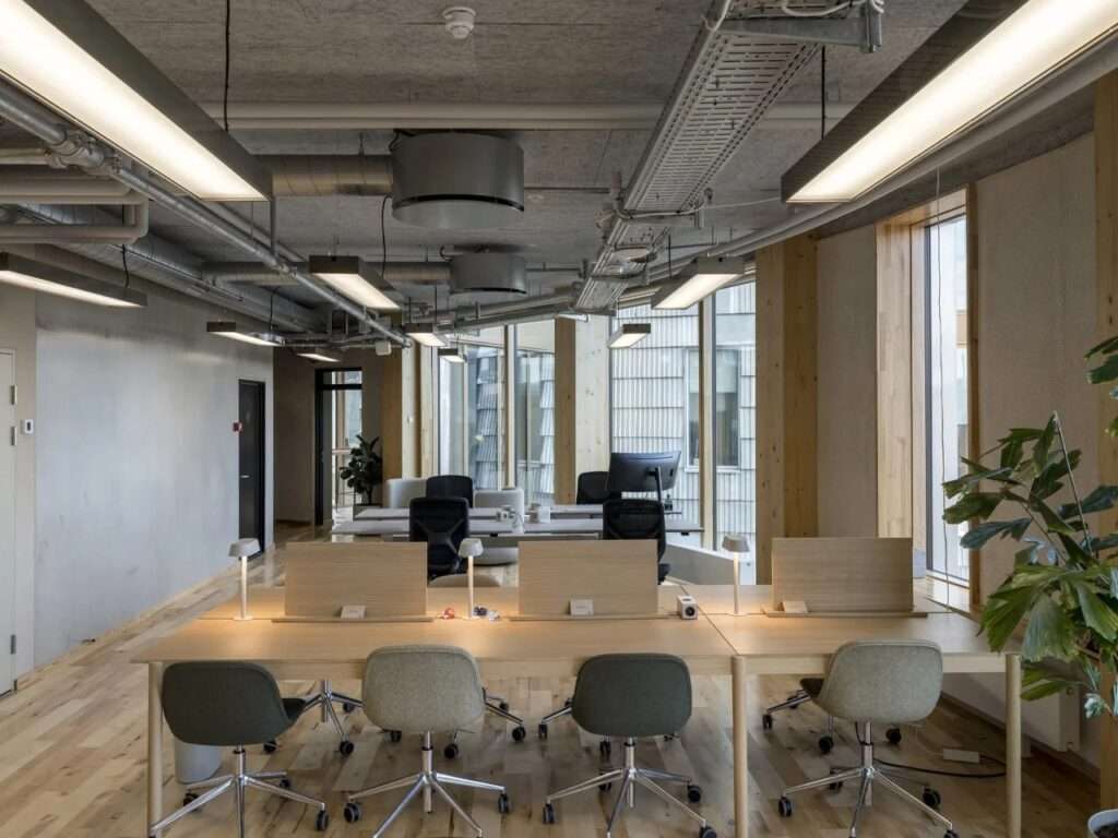 Modern open-plan office interior inside the TRAE building featuring exposed glulam timber columns, raw concrete ceilings, and wooden desks.