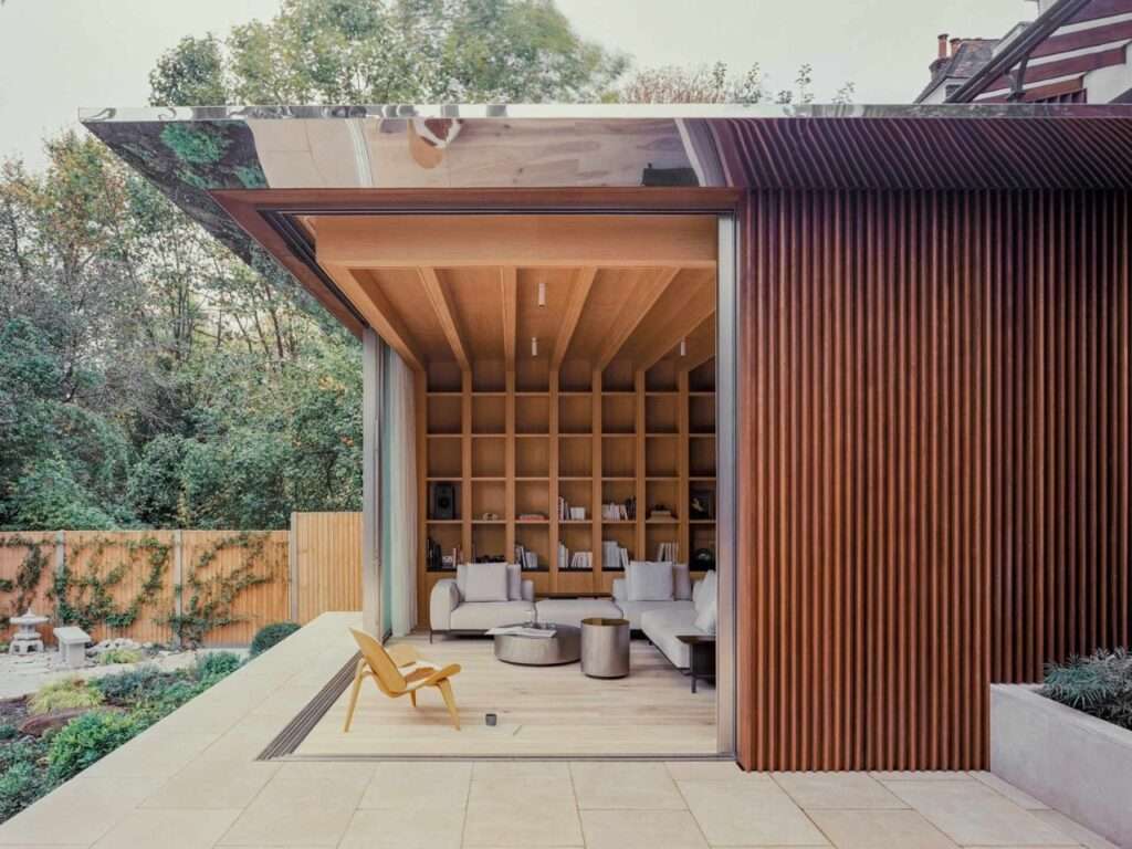 Open sliding glass doors showing a seamless transition from a limestone patio into a wood-paneled living room with built-in bookshelves.