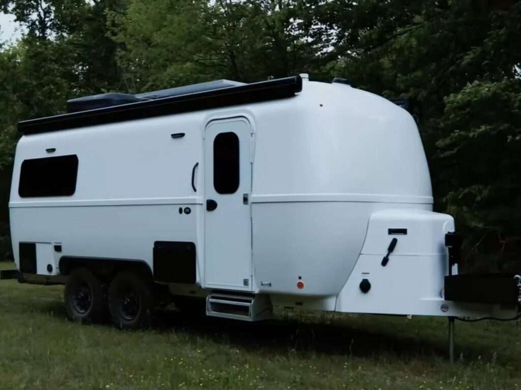 Detailed 3/4 view of the white Oliver Apex X23 fiberglass shell showing the entry door and tandem axle wheels.