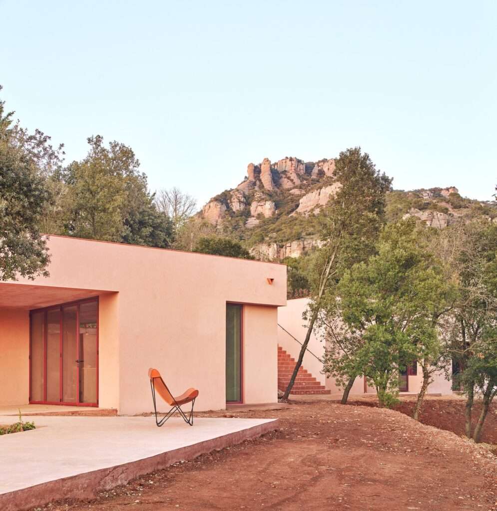 Monochromatic reddish concrete exterior of Casa Sota la Mola by Twobo Arquitectura, showing fragmented volumes integrated into the terrain at the foot of La Mola mountain.