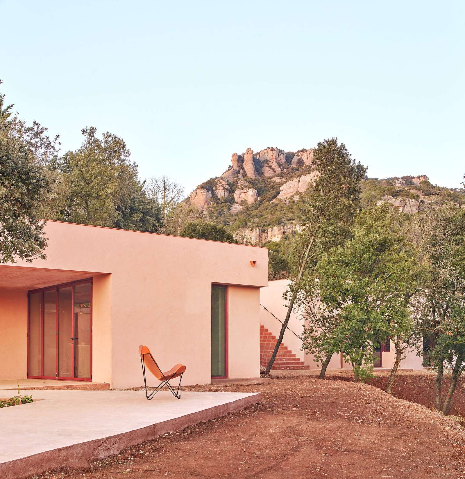 Monochromatic reddish concrete exterior of Casa Sota la Mola by Twobo Arquitectura, showing fragmented volumes integrated into the terrain at the foot of La Mola mountain.