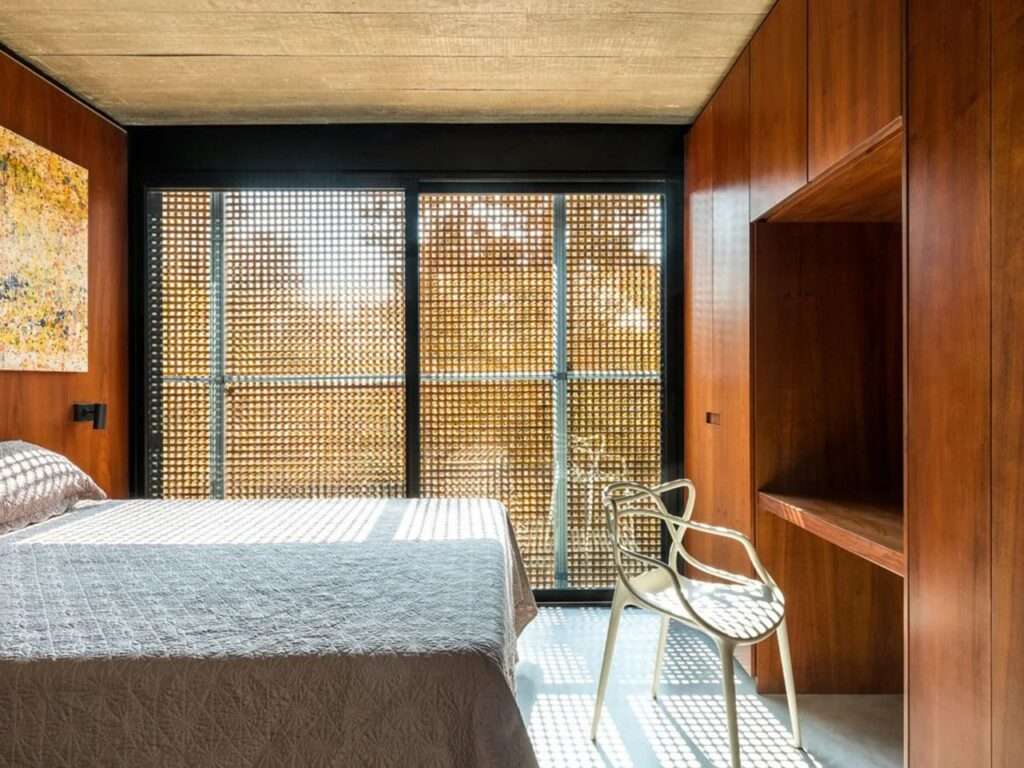 Bedroom in House 17-JB featuring a light-filled space filtered through a perforated wooden screen and warm wood paneling.
