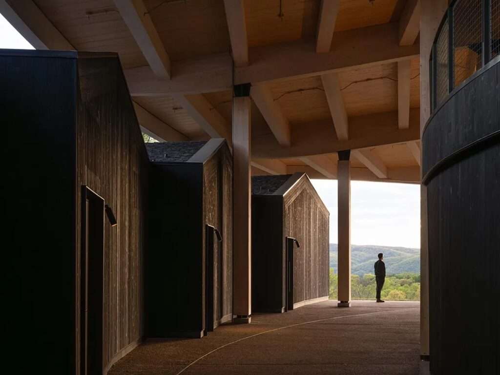 Architectural walkway under the timber roof structure next to dark-stained wood ancillary support buildings at the Scripps Theater Center.