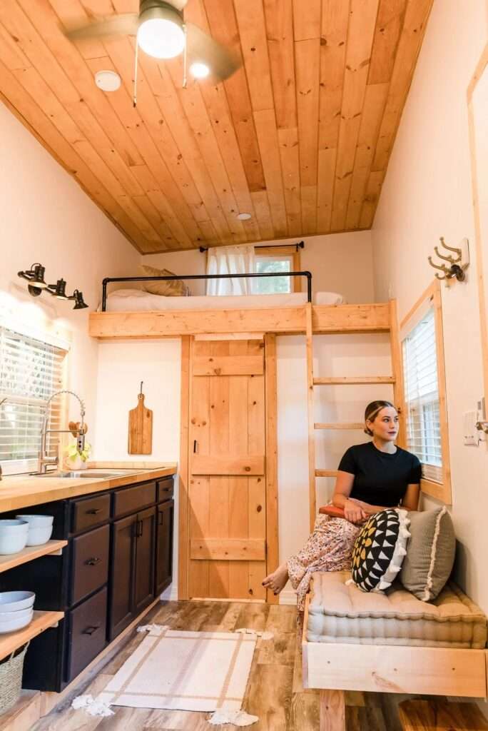 Interior shot of the Tulsi tiny house kitchen with black cabinetry, wood countertops, and an adjacent built-in bench under a window.