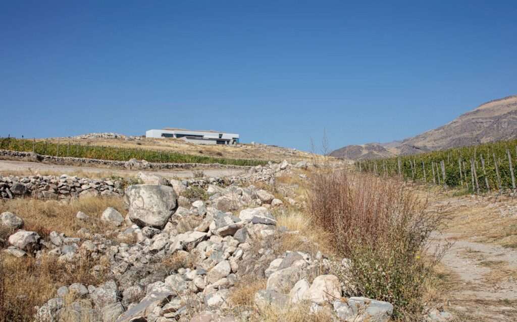 Distant landscape view of the low-density horizontal villa embedded on a high plateau surrounded by rocky terrain and terraced vineyards in Vayots Dzor, Armenia.