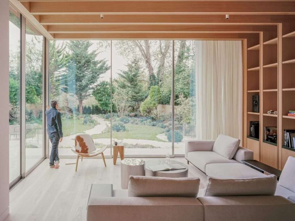 Interior of a modern living room looking out through floor-to-ceiling windows onto a lush green garden in Hampstead.