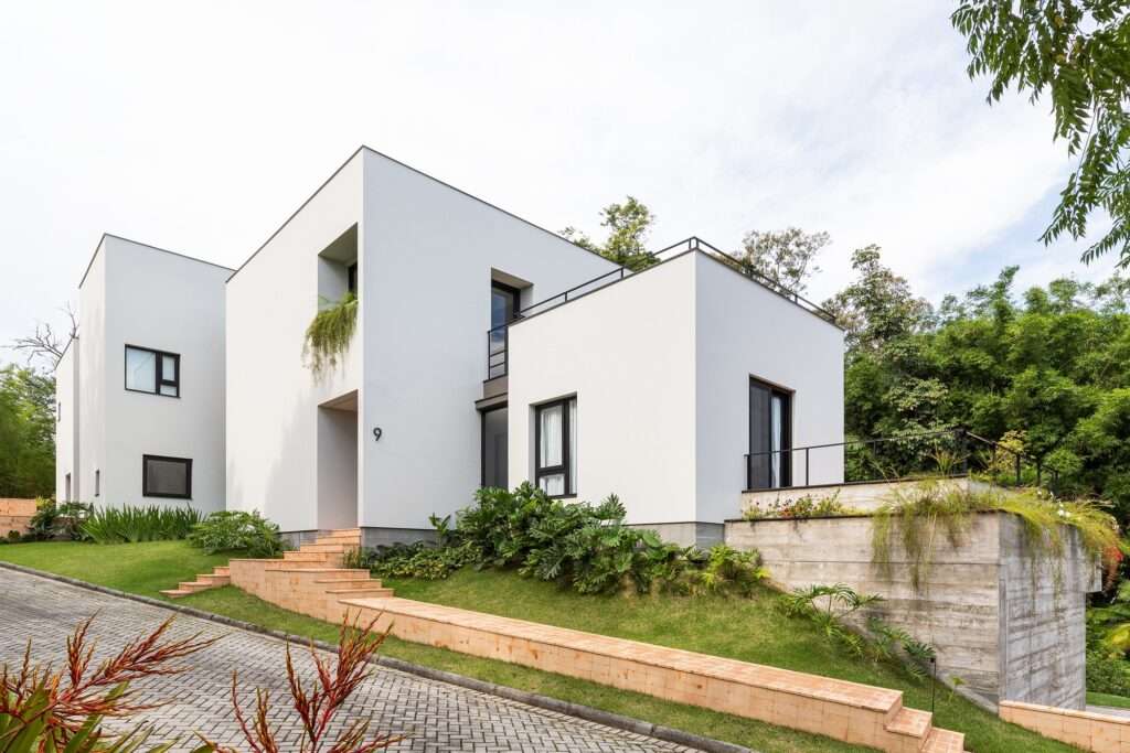 Paved driveway alongside terraced brick steps leading up the slope to the entrance of a modern white concrete home.