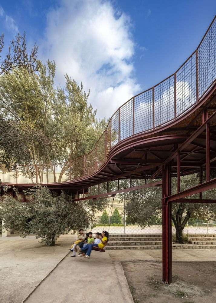 Children enjoying a large swing attached to an elevated red steel frame structure in a benched garden courtyard.