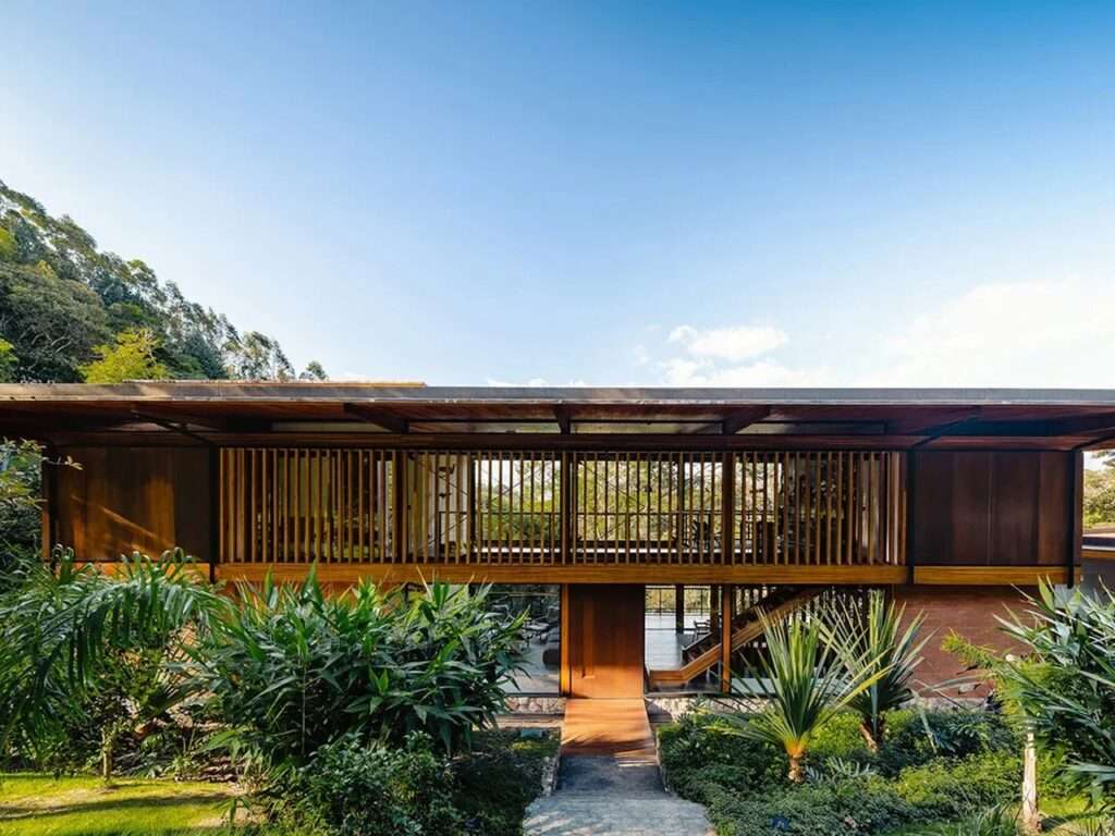 Frontal view of the house entrance featuring vertical wooden slats and lush tropical landscaping.