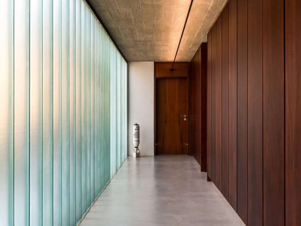 A long corridor in House 17-JB with a translucent glass wall on one side and dark wood paneling on the other.