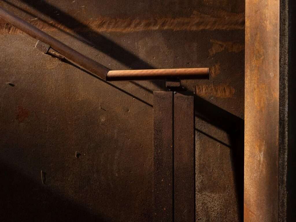 Macro shot of a rusted steel handrail and shadows on a textured metal surface at the lookout.