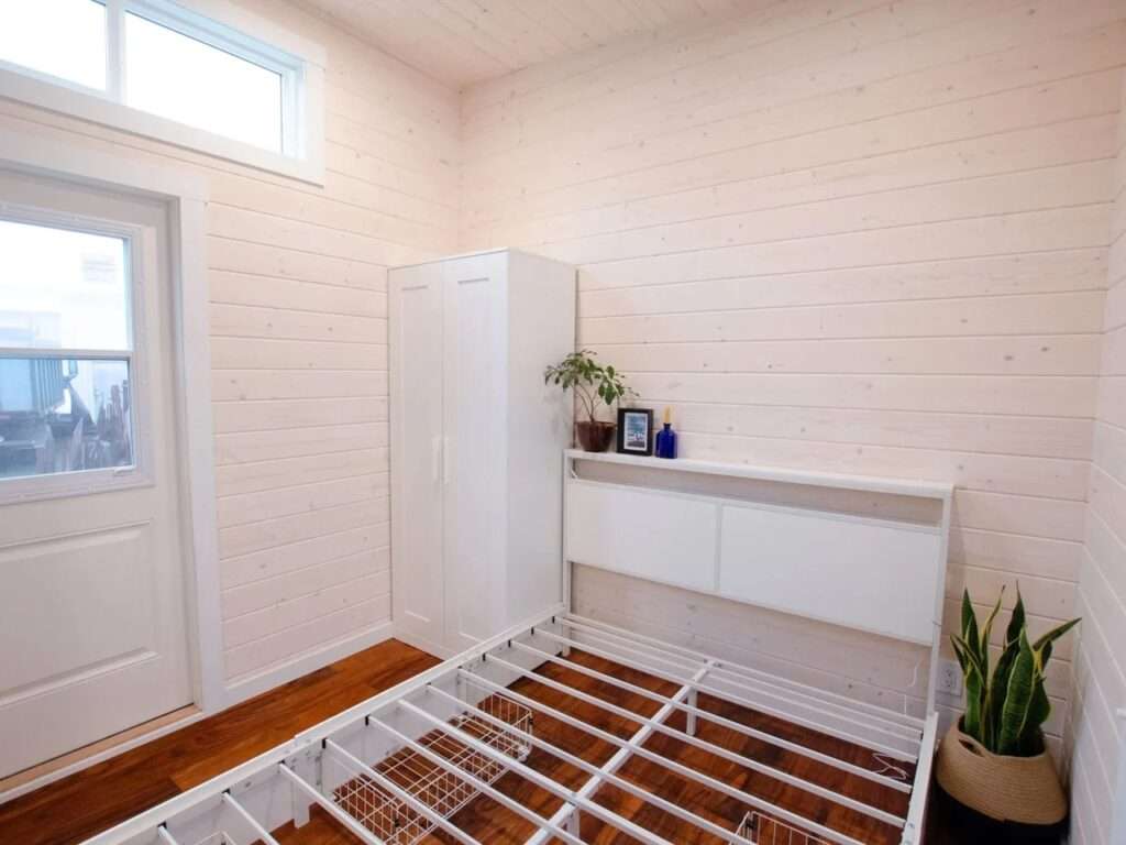 Light-filled main floor bedroom frame with built-in metal slats for storage underneath, a white wardrobe, and a private exterior glass door.