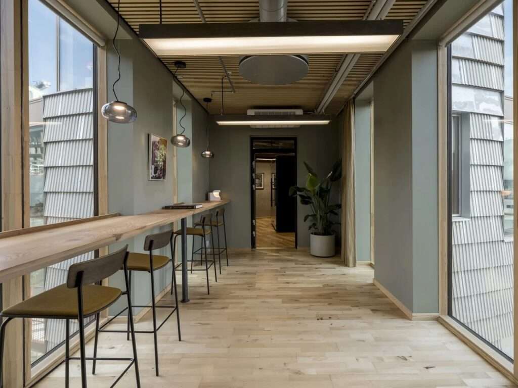 Co-working corridor inside TRAE building with a long wooden bar counter, bar stools, and a close-up view of the exterior shingle facade through the window.