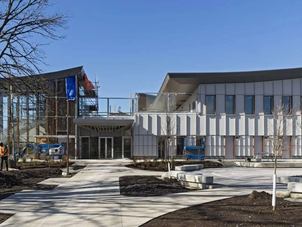 Front entrance of Marpole Community Centre featuring concrete walkways, newly planted greenery, and the textured vertical facade treatment.