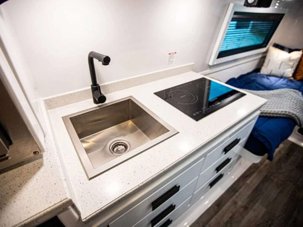 Modern interior of Oliver Apex X23 showing a white countertop with an induction cooktop, stainless steel sink, and black faucet.