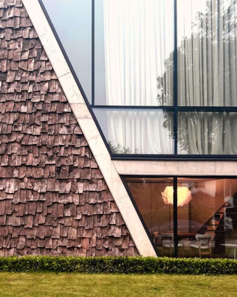 Close-up of the front facade featuring a triangular wooden shingle wall next to trapezoidal and rectangular glass windows.