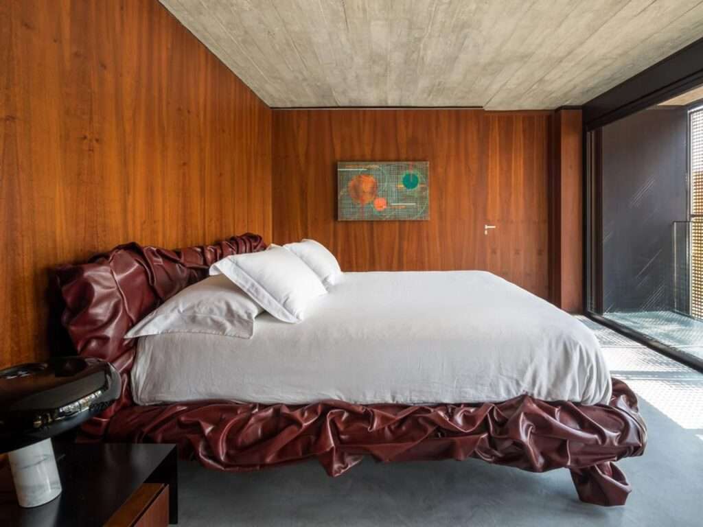 Luxurious master bedroom in House 17-JB with deep red leather bed frame and dark wood walls.