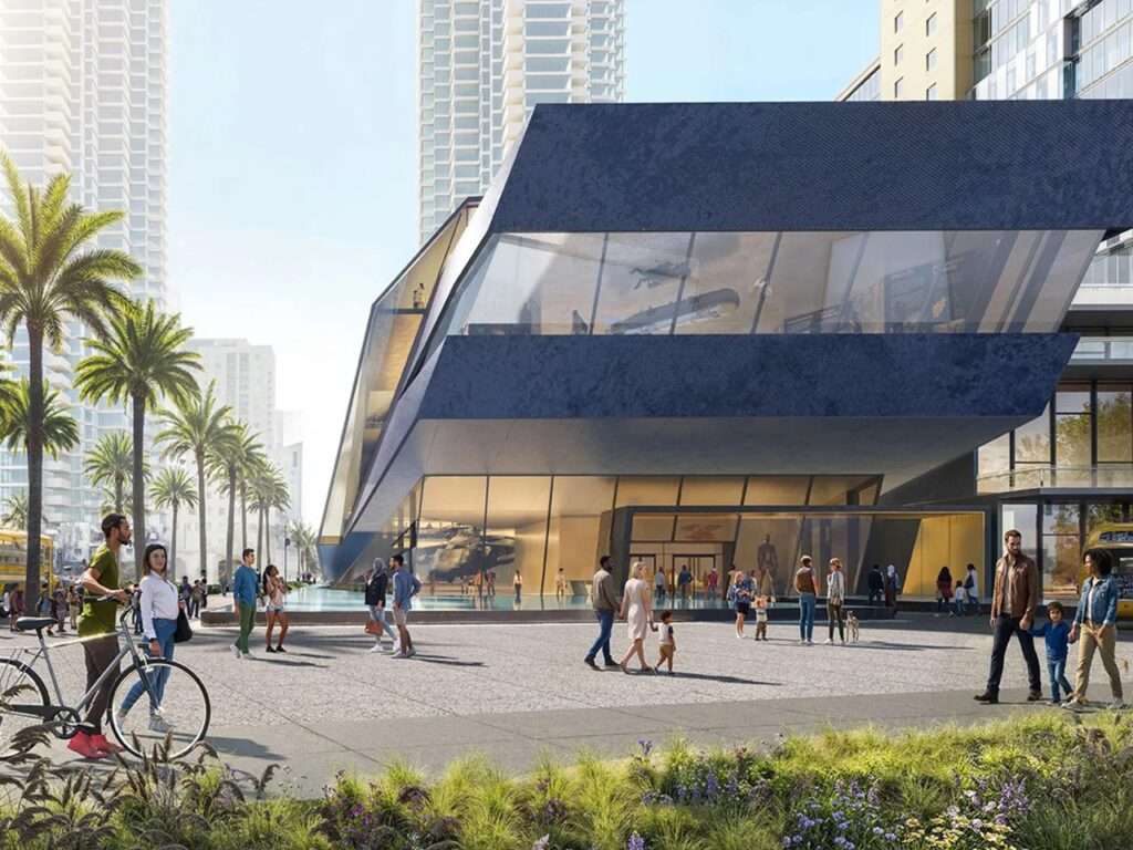 Plaza view of the main entrance to the Navy SEAL Museum San Diego, highlighting a transparent glass ground floor, a large window revealing interior naval exhibitions, and visitors walking on the surrounding paved esplanade.
