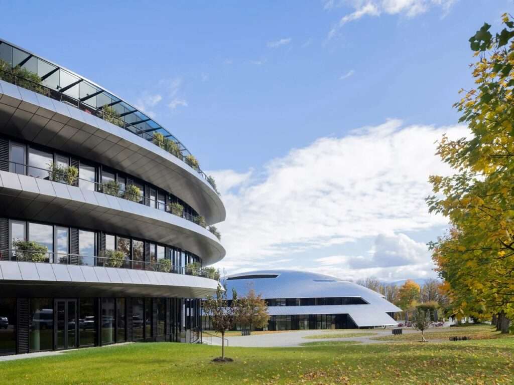 Low-angle exterior shot capturing the reflective metal overhangs of the Philo Center with the metallic dome of Carnal Hall visible in the background under a blue sky.