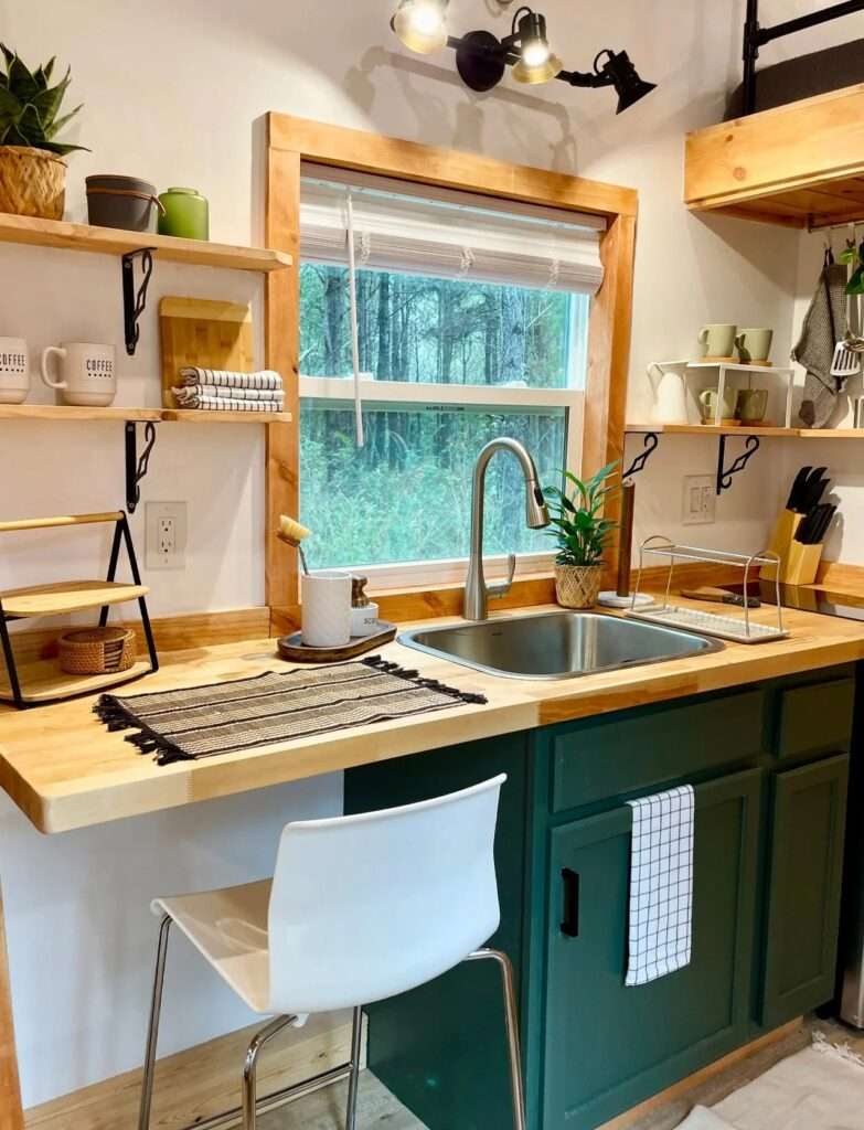 Compact kitchen in Rasa tiny home featuring butcher block countertops, a stainless steel sink, and forest green cabinetry.